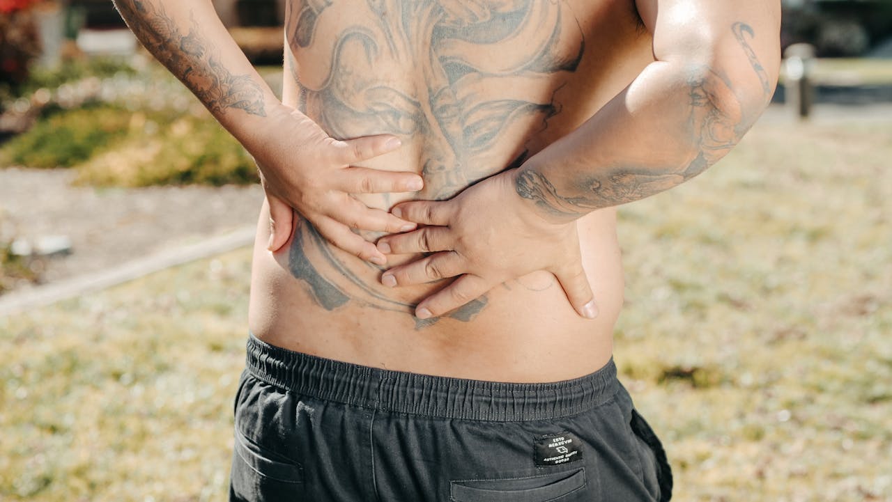 A man holds his low back outdoors, showing discomfort.